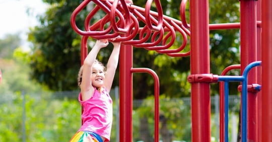 young girl hanging on monkey bars with a strained look on her face