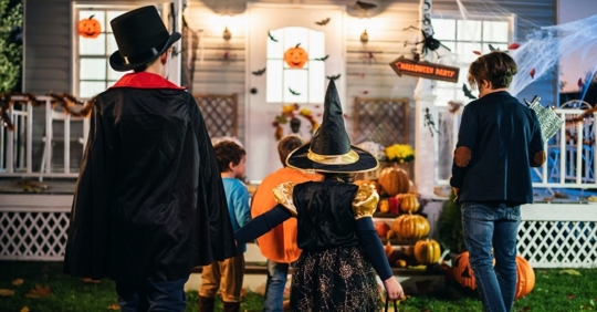 child dressed as a magician holding the hand of a child dressed as a witch walking up to the front door of a house