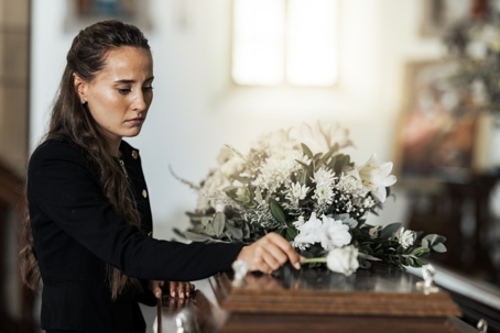 Funeral, sad and woman with flower on coffin after loss of a loved one.